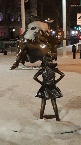 Fearless Girl Statue standing up to the Charging Bull in the snow