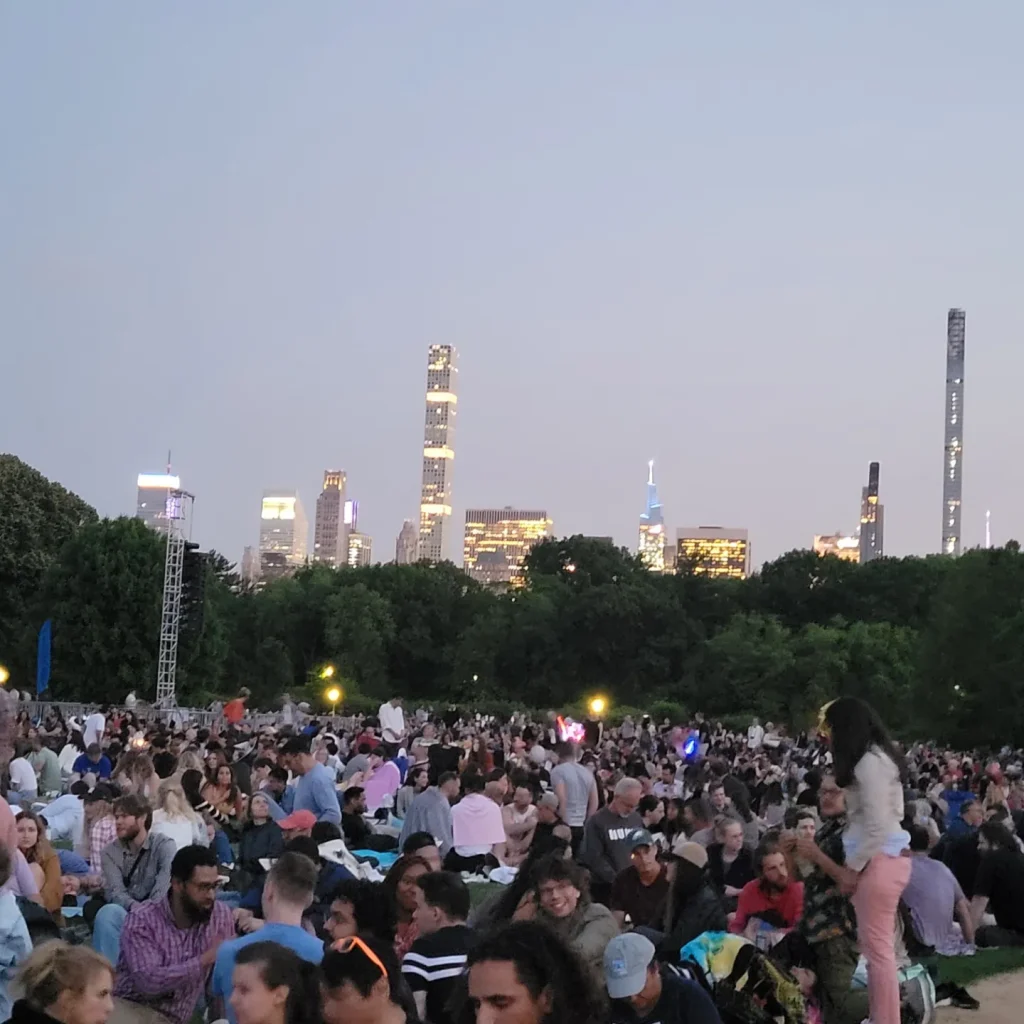 Attendees at a concert at the Great Lawn in Central Park surrounded by the New York skyline 