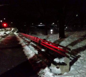 Path through the snow in with traffic light reflecting off benches in Central Park at Night