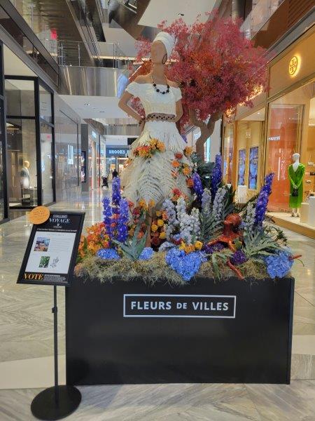 Puerto Rico floral mannequin in a white dress and headress, surrounded by colorful trees and flowers