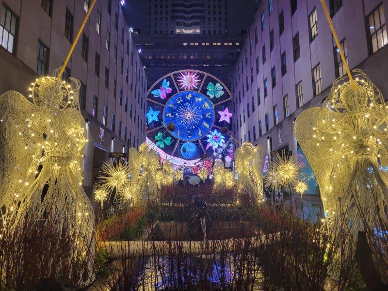 View of the Saks Holiday Light Show Carousel on the Saks store from Rockefeller Center through the holdiay angel decorations