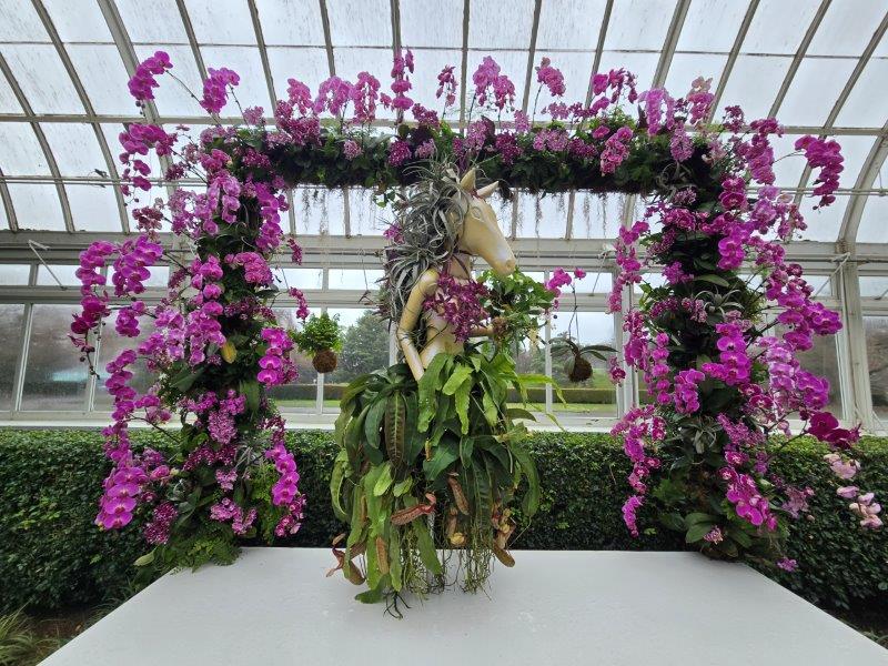 Horse mannequin on a platform wearing a green orchid dress with a pink orchid frame as a backdrop 